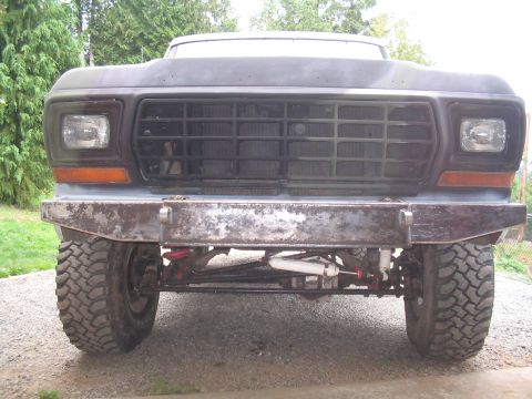 1979 Ford Bronco - The front grille and custom bumper of a 1979 Ford Bronco are visible, along with its large off-road tires.