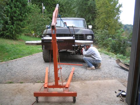 1979 Ford Bronco - Front view of a lifted dark-colored square-body Ford truck parked on a gravel driveway with a shop-built bare-steel bumper test-fitted acro…