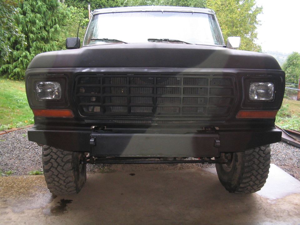 Front view of camo-painted lifted Ford truck with custom flat steel bumper on wet concrete