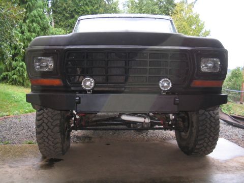 1979 Ford Bronco - Head-on front view of a lifted flat-black full-size Ford Bronco with a white roof, sitting on a concrete driveway with a fabricated flat-pl…