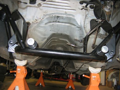 1992 Ford Mustang - The underside of a vehicle is shown with a black tubular brace installed and supported by orange jack stands.