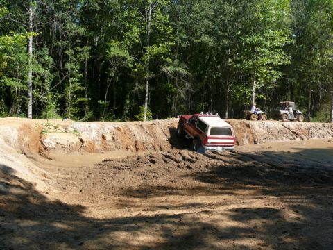 1988 Ford Bronco - Ford Bronco navigates a muddy obstacle course with ATVs nearby.