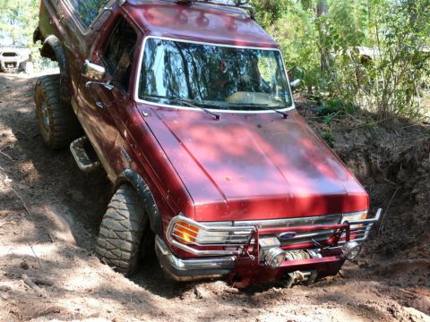 1988 Ford Bronco - This red Ford Bronco is navigating a challenging off-road trail, with another vehicle visible in the distance.
