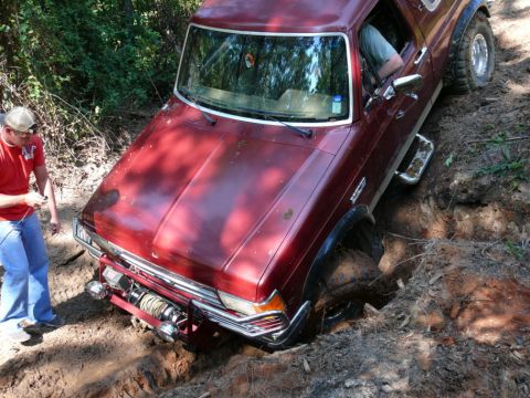 1988 Ford Bronco - A red Ford Bronco is stuck in a deep dirt ditch, with a person standing outside observing.