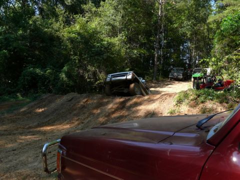 1988 Ford Bronco - Several off-road vehicles navigate a dirt track through a wooded area.
