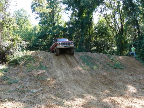 1988 Ford Bronco - A red 1980s Ford Bronco navigates an off-road course, ascending a steep dirt embankment.