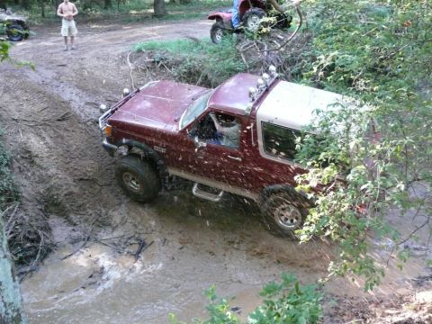 1988 Ford Bronco - Ford Bronco tackles a challenging muddy off-road course, with an ATV visible in the distance.