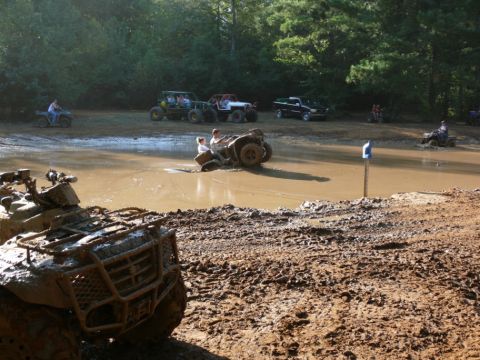 1988 Ford Bronco - Several off-road vehicles navigate a muddy waterhole on a sunny day.
