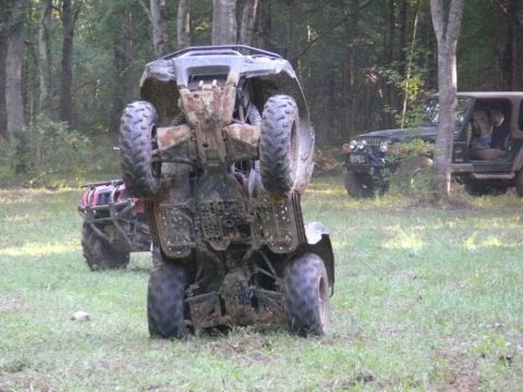 1988 Ford Bronco - A four-wheeler is tipped onto its side in a grassy area, with other off-road vehicles visible in the background.
