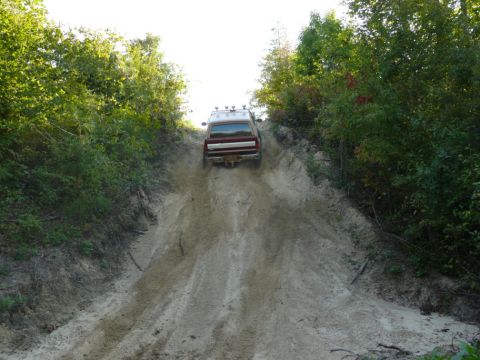1988 Ford Bronco - A vehicle navigates a challenging incline on a dirt trail surrounded by dense foliage.