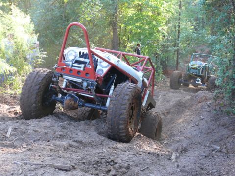 1988 Ford Bronco - An off-road vehicle navigates a muddy trail, with another vehicle following behind in the woods.