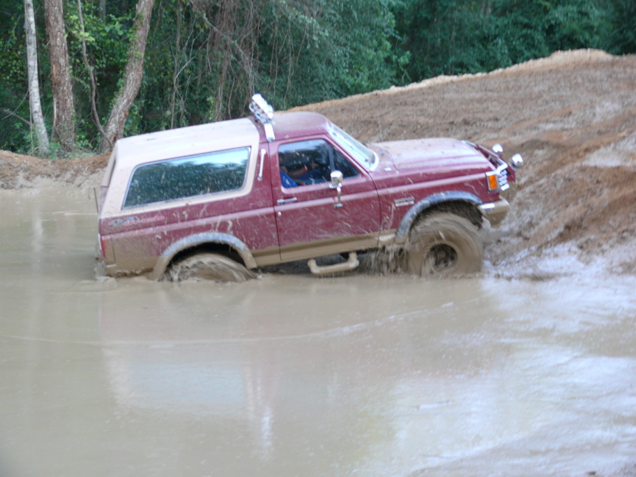 Maroon Ford Bronco with a tan top stuck in mud, viewed from the front-right