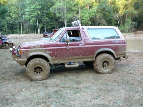 1988 Ford Bronco - Mud-covered 1988 Ford Bronco navigates an off-road park with other ATVs visible in the background.
