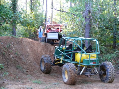 1988 Ford Bronco - Two off-road vehicles navigate a dirt trail in a wooded area.