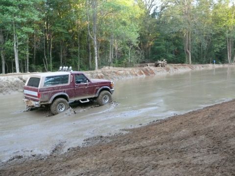 1988 Ford Bronco - A maroon Ford Bronco navigates a muddy track, with an ATV visible in the background.