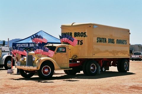 1981 Kenworth W900A - A vintage yellow semi-truck and trailer, adorned with numerous American flags, is parked outdoors under a clear blue sky.