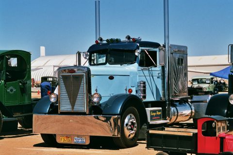 1981 Kenworth W900A - A classic Peterbilt 359 truck is displayed outdoors with other vehicles and a large building in the background.