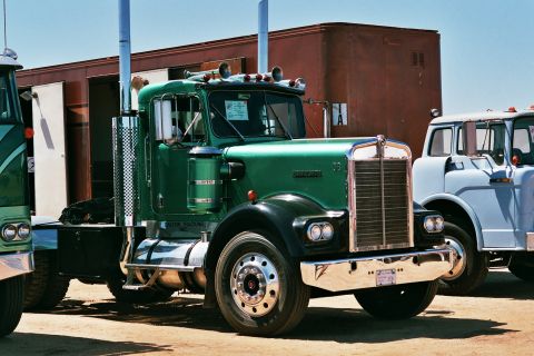 1981 Kenworth W900A - A green semi-truck is parked outdoors with other trucks nearby under a clear blue sky.