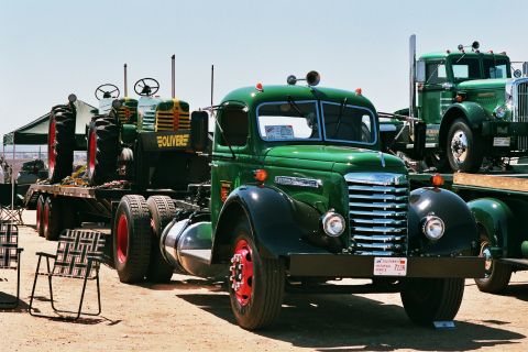 1981 Kenworth W900A - A green truck tows a vintage Oliver tractor, with another truck in the background.