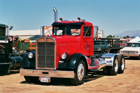 1981 Kenworth W900A - A classic red semi-truck is parked outdoors with other vehicles in the background under a clear blue sky.