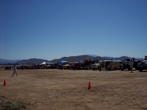 1981 Kenworth W900A - A variety of trucks and cars are parked in a long line on a dirt lot, with mountains in the background.