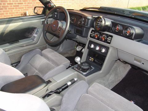 1998 Ford Crown Victoria - Gray cloth interior of a Ford coupe showing the airbag steering wheel, manual shifter and a cluster of aftermarket gauges.