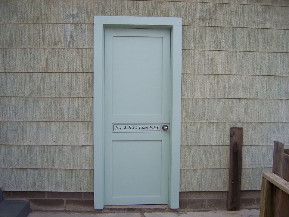 Light blue door on a house with horizontal siding. Plaque reads 'Nana & Bubba's Forever 1958'