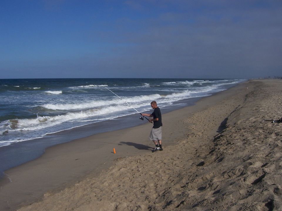 Man fishing on a sandy beach with waves crashing