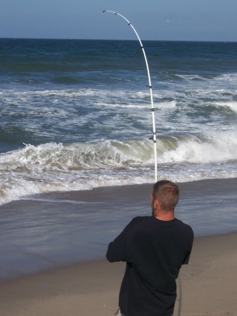 1991 Ford Bronco - A man stands on the shore, casting a white fishing rod into the ocean waves.