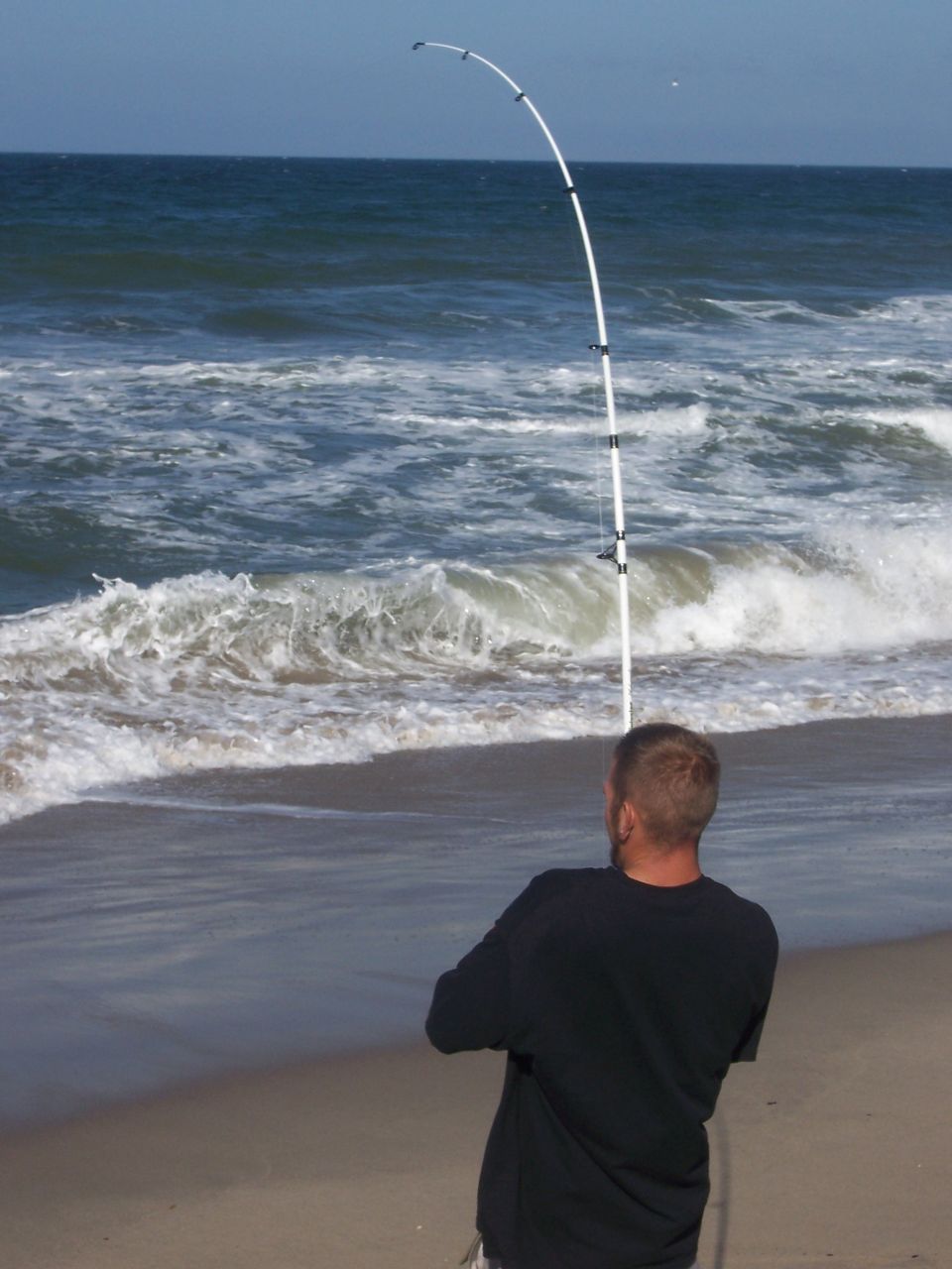 Man fishing on beach with white fishing rod