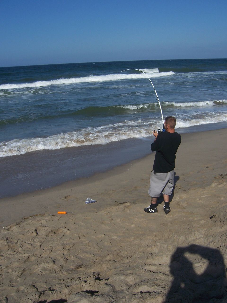 Man fishing with a rod and reel on a sandy beach with waves in the background