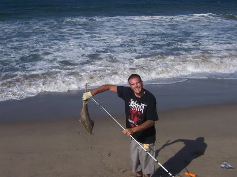 1991 Ford Bronco - A smiling man proudly displays a fish he caught while fishing on the beach, with the ocean waves crashing behind him.