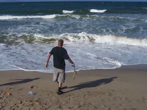 1991 Ford Bronco - A man walks along the shore, holding a small fish he has caught, with the ocean waves crashing behind him.