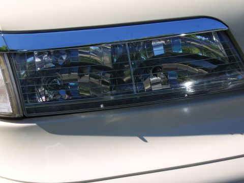 1996 Mercury Grand Marquis - Close-up of a white car's front headlight assembly with a clear multi-reflector lens, showing 'Ford' and 'RH' molding text near the bottom…