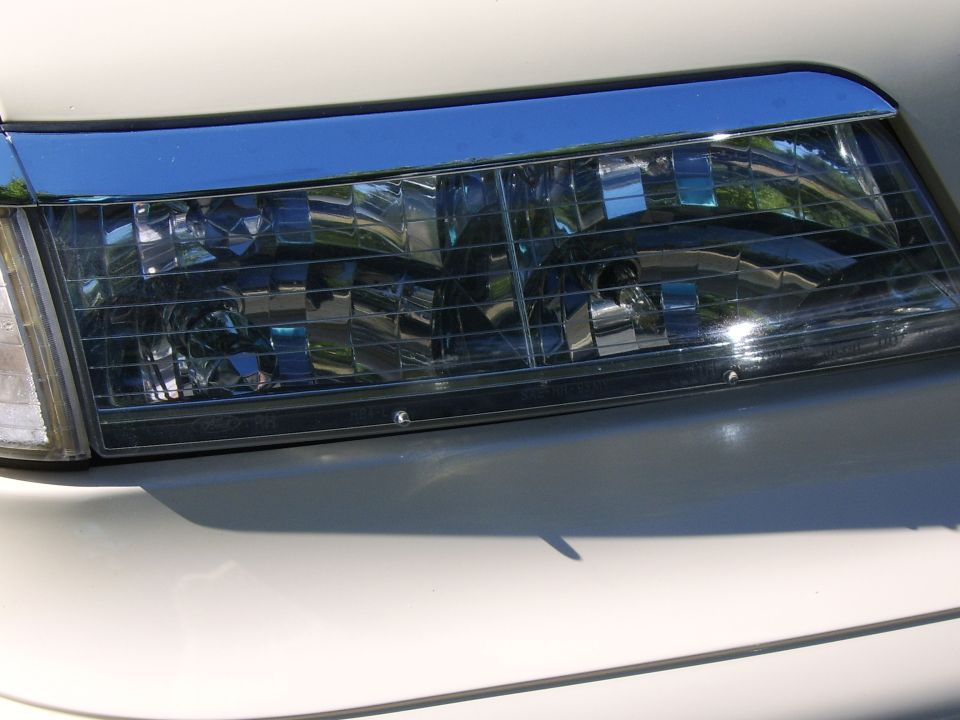 Close-up of a white car's headlight with clear gridded lens and chrome reflectors