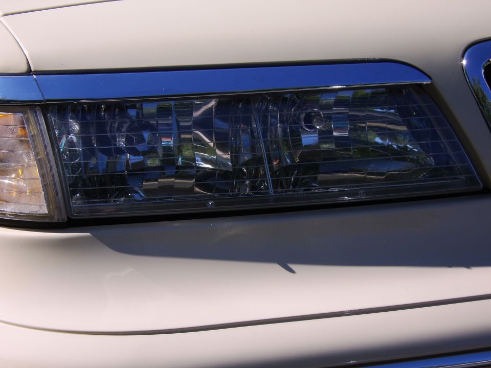 Close-up of a cream sedan's driver-side headlight with amber turn signal and chrome trim.