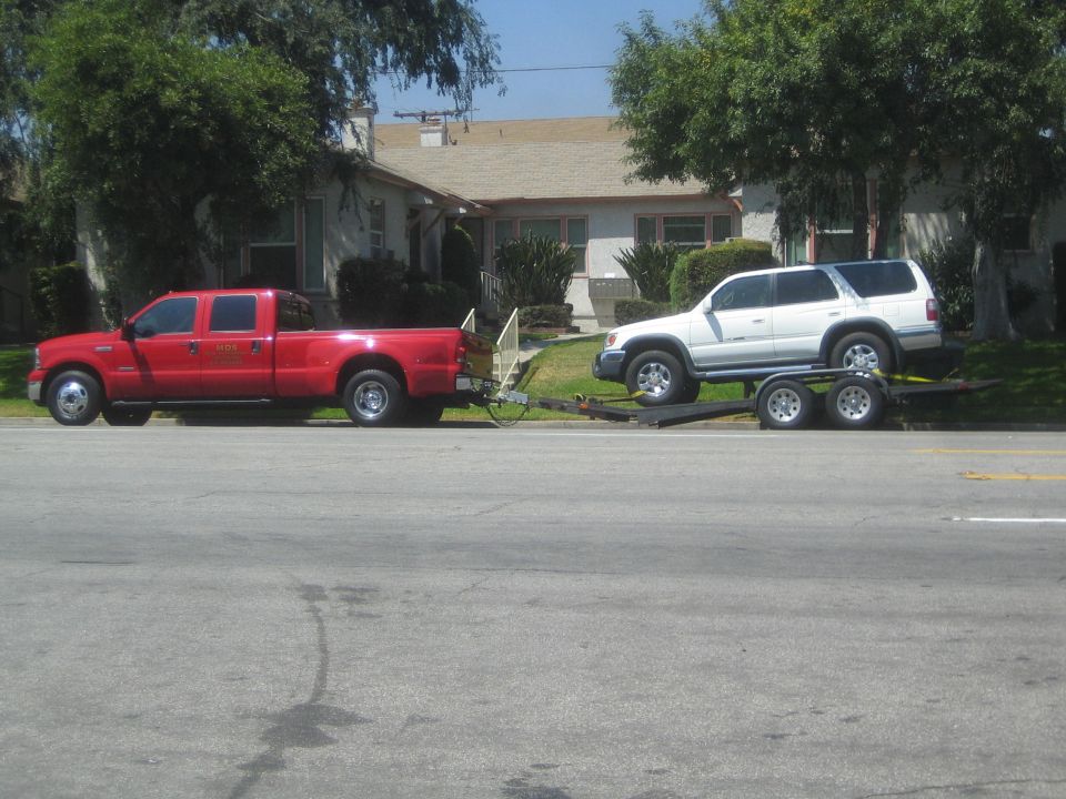Red pickup truck towing white SUV on trailer, side view