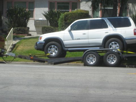 1968 Ford Mustang - A white SUV is loaded onto a trailer, ready for transport on a sunny day.