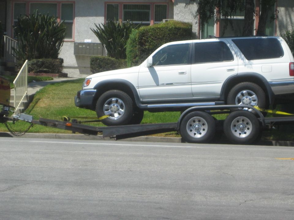 White SUV being towed on a double-axle trailer, parked on the side of a residential street