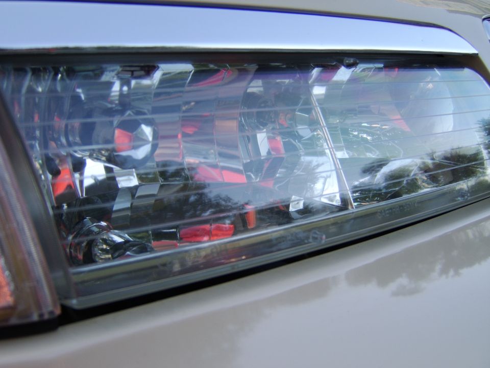 Close-up of a clear headlight lens on a silver car with amber turn signal