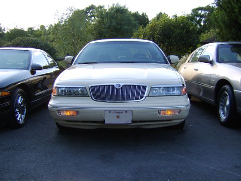 1996 Mercury Grand Marquis - Front view of a cream/beige Mercury Grand Marquis sedan with a chrome vertical-slat grille, Mercury emblem, amber turn signals lit, and a M…