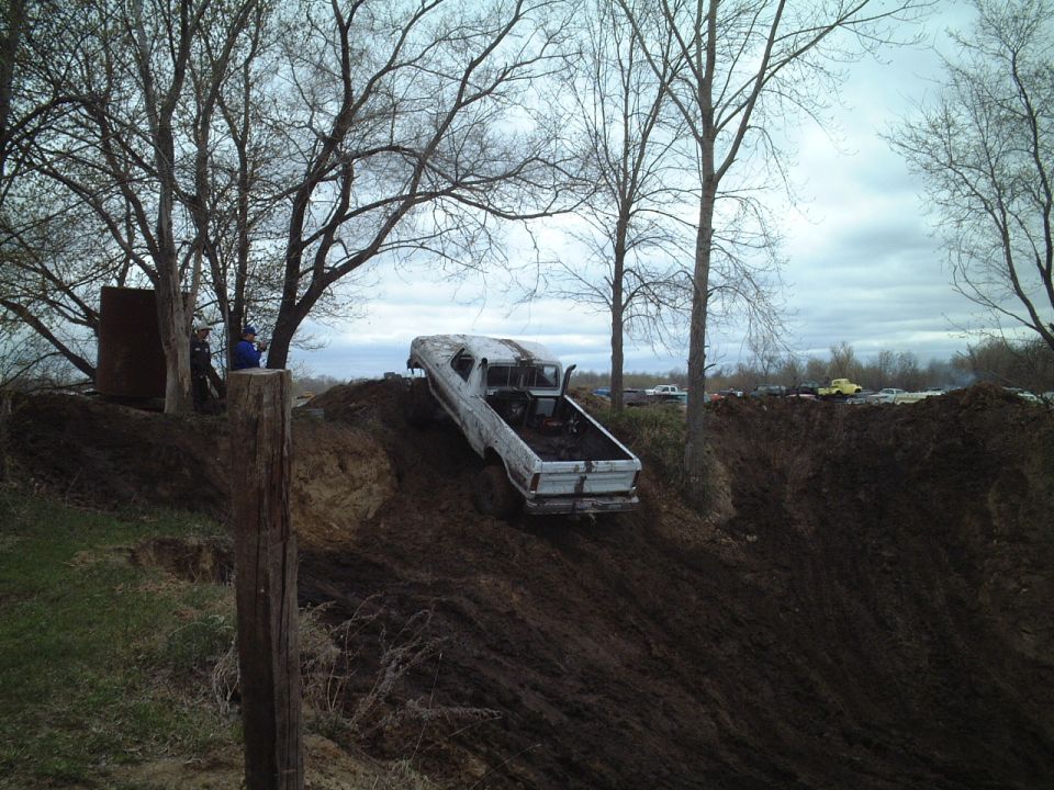 White pickup truck covered in mud climbing a steep dirt hill at an off-road event