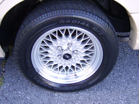 1996 Mercury Grand Marquis - Close-up of a silver multi-spoke mesh alloy wheel with a black Ford center cap, mounted with a Cooper Cobra Radial G/T raised-white-letter…