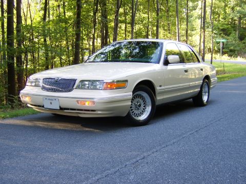 1996 Mercury Grand Marquis - A cream/white 1990s Mercury Grand Marquis full-size sedan photographed from the front three-quarter angle, parked on a paved road in front…