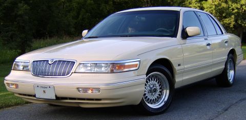 1996 Mercury Grand Marquis - A cream/beige Mercury Grand Marquis full-size sedan shown from a front three-quarter angle, featuring a chrome waterfall grille, chrome-lip…