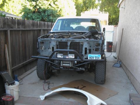 1990 Ford Bronco - This white SUV is undergoing modifications, with its front end disassembled to reveal the engine and a winch mounted on the bumper.