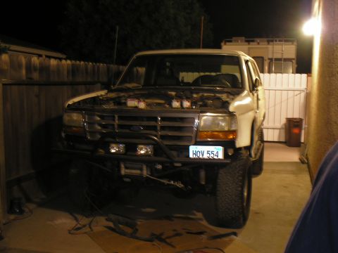 1990 Ford Bronco - A white Ford Bronco sits in a driveway with its hood up, revealing the engine bay.