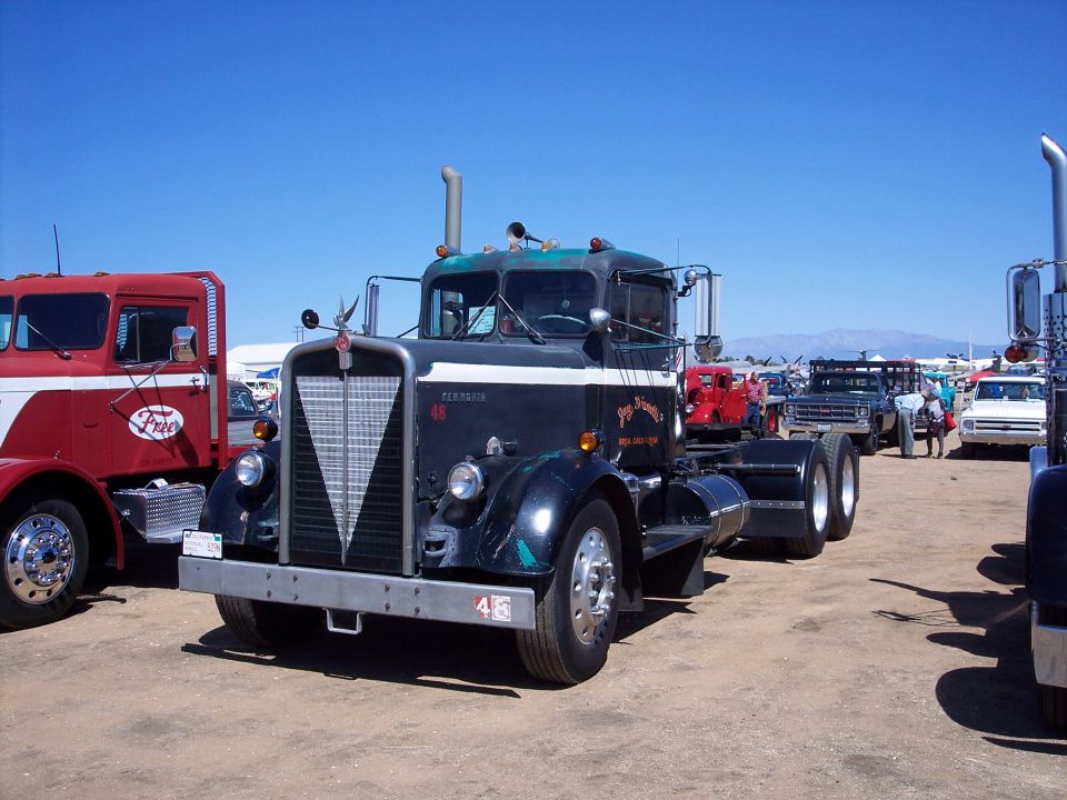 Black vintage Kenworth day-cab semi tractor, 3/4 front view at a dirt-lot truck show