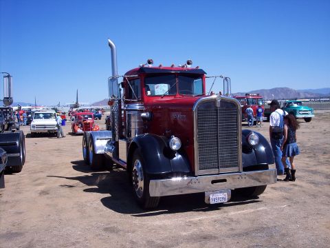 1981 Kenworth W900A - A classic red and black semi-truck is parked outdoors with other vehicles and airplanes in the background.
