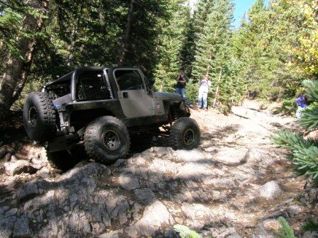 1995 Ford Bronco - A modified Jeep Wrangler navigates a challenging rocky path through a forest.